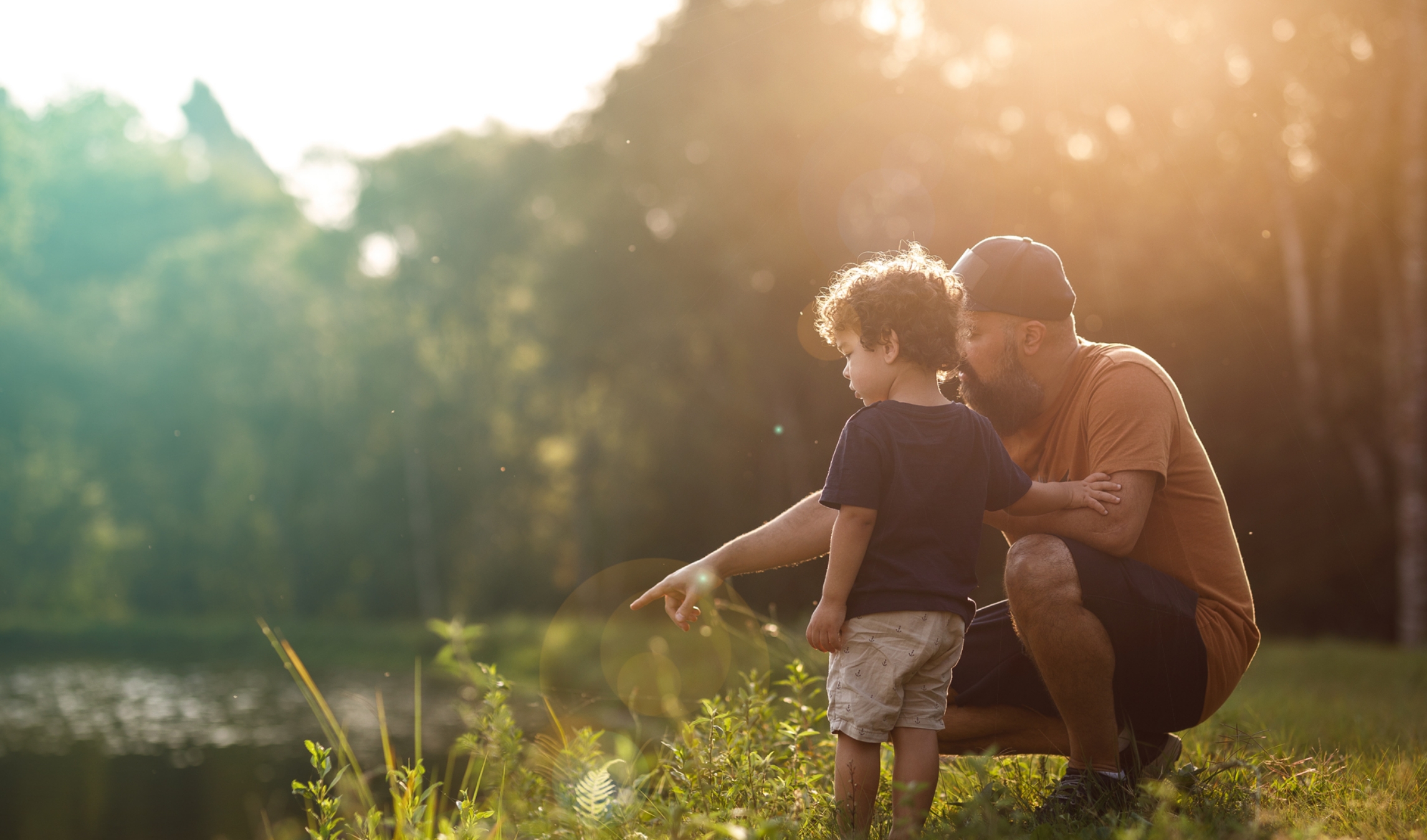 father points to into the lake to show his young son something in the water