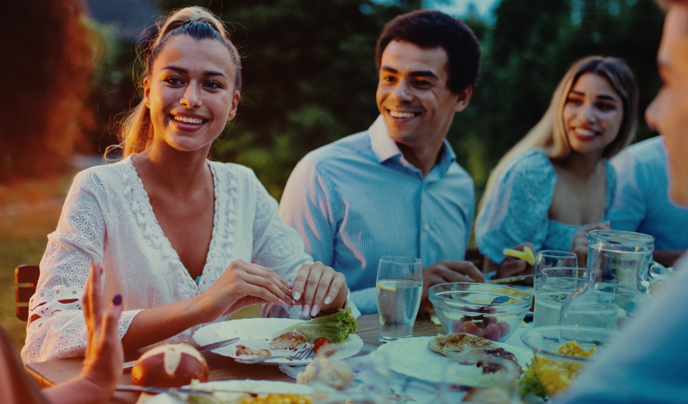friends smiling and conversing around a table outdoors at sunset