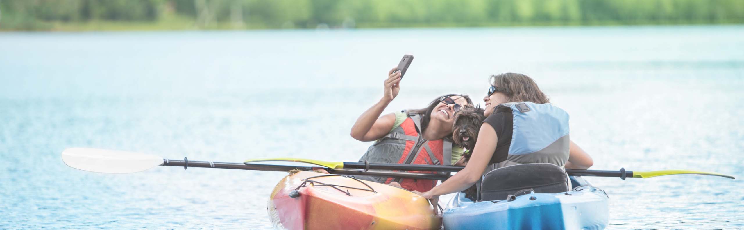 friends pose for a picture together in kayaks on the lake with their dog