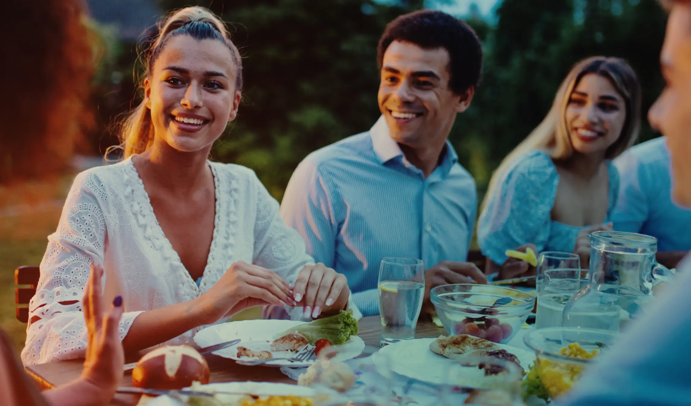 friends smiling and conversing around a table outdoors at sunset