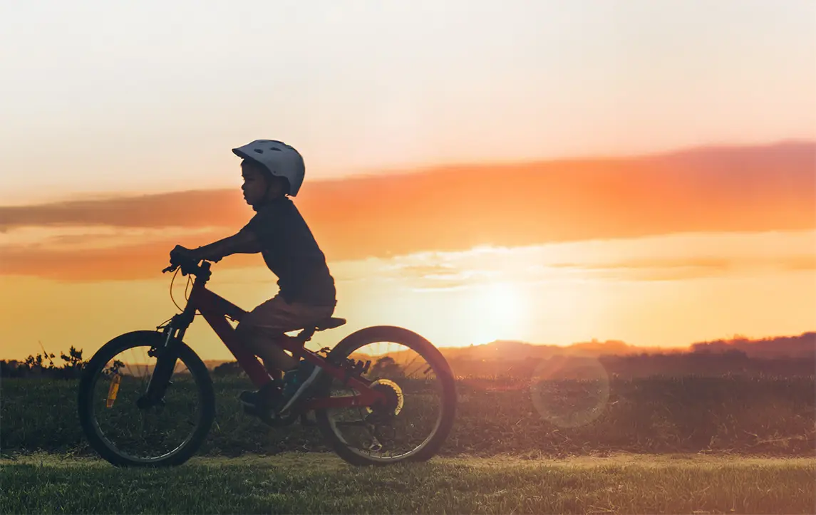 boy riding a bike along grass at sunset along the plains